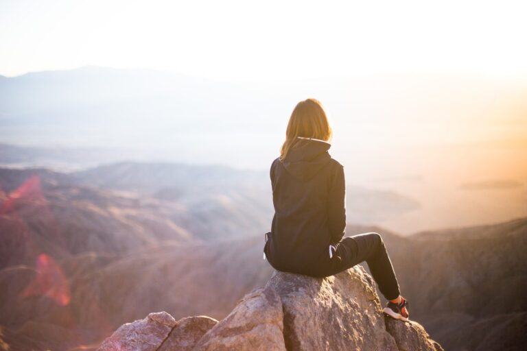A woman sitting on a rock overlooking mountains, reflecting on what she has learned about rewiring her brain in the moment.